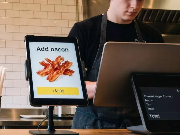 Customer-facing display next to the register showing Add bacon, +$1.99